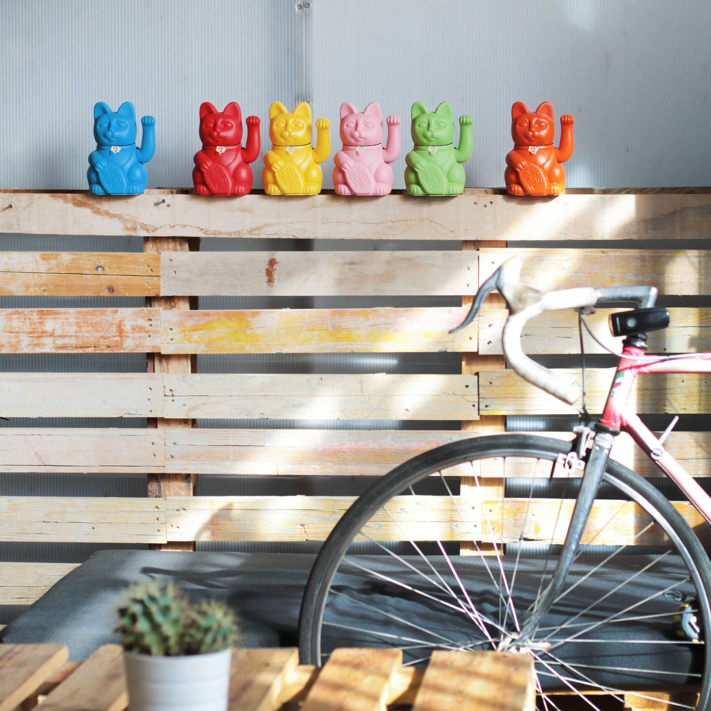 Verschiedene Maneki Nekos sind auf einem Zaun aufgereiht und winken dem Betrachter zu