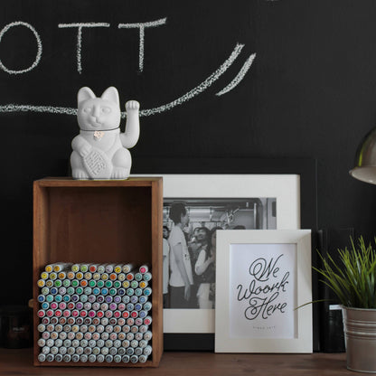 Eine weiße Lucky Cat steht dekorativ auf einem Sideboard umgeben von anderen stilvollen Dekoartikeln in weiß